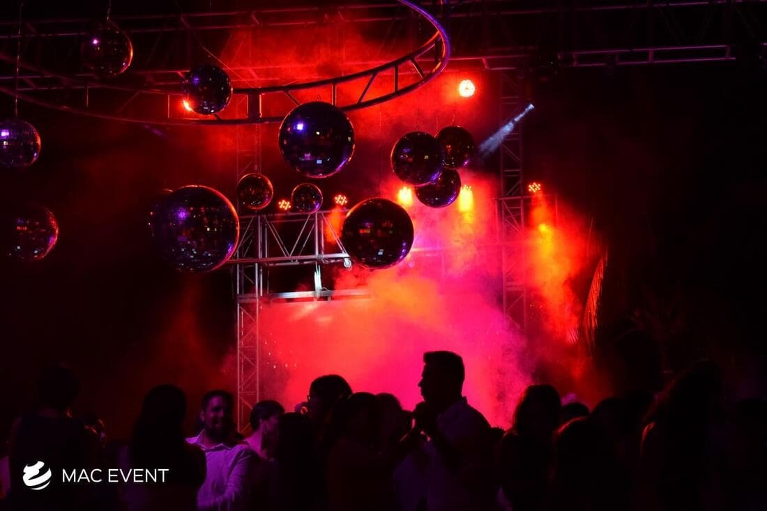A dance floor filled with people enjoying a party under an intense red lighting display, with disco balls reflecting the glow and enhancing the celebratory mood.